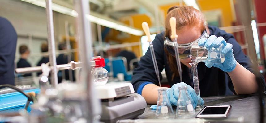 在RWU布里斯托尔校区的实验室里，一名戴着护目镜的学生小心地从玻璃容器中倒出液体